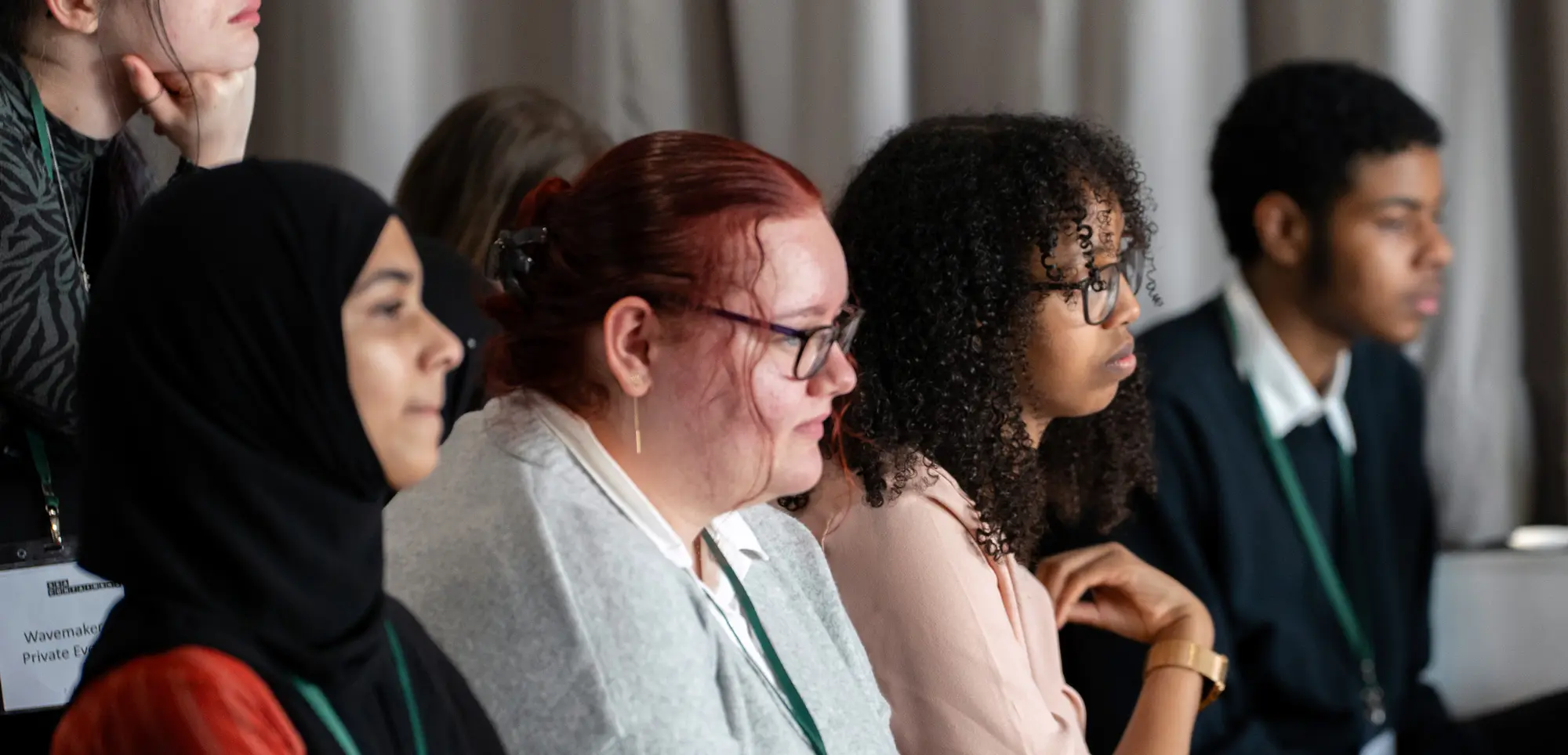 Three students sit at a desk listening to a speaker