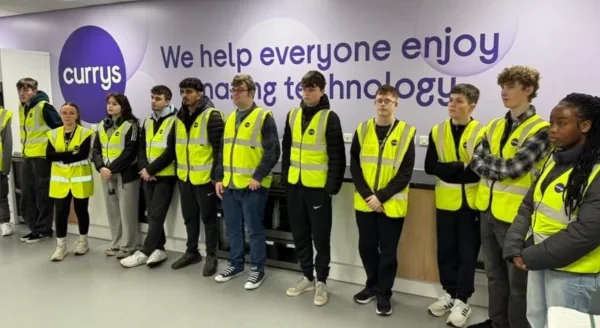 Students in hi viz jackets standing in front of a Currys branded wall
