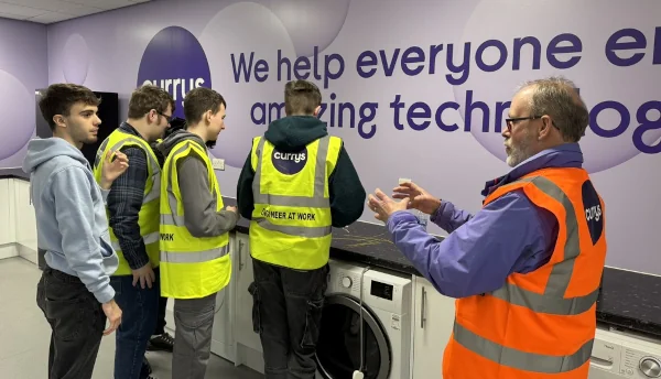 Students in hi viz jackets standing in front of a Currys branded wall